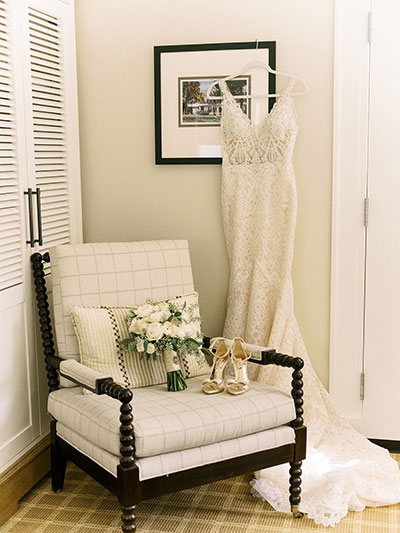 Wedding dress next to armchair with bouquet and wedding shoes