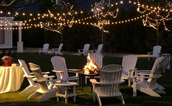 Lounge chairs around a firepit under string lights -  Fire Pits
