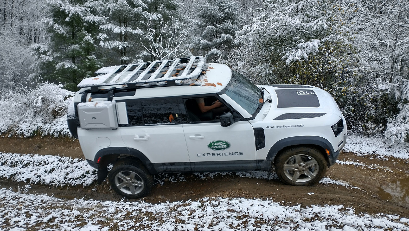 White Land Rover Defender 110 navigating a snowy, muddy trail