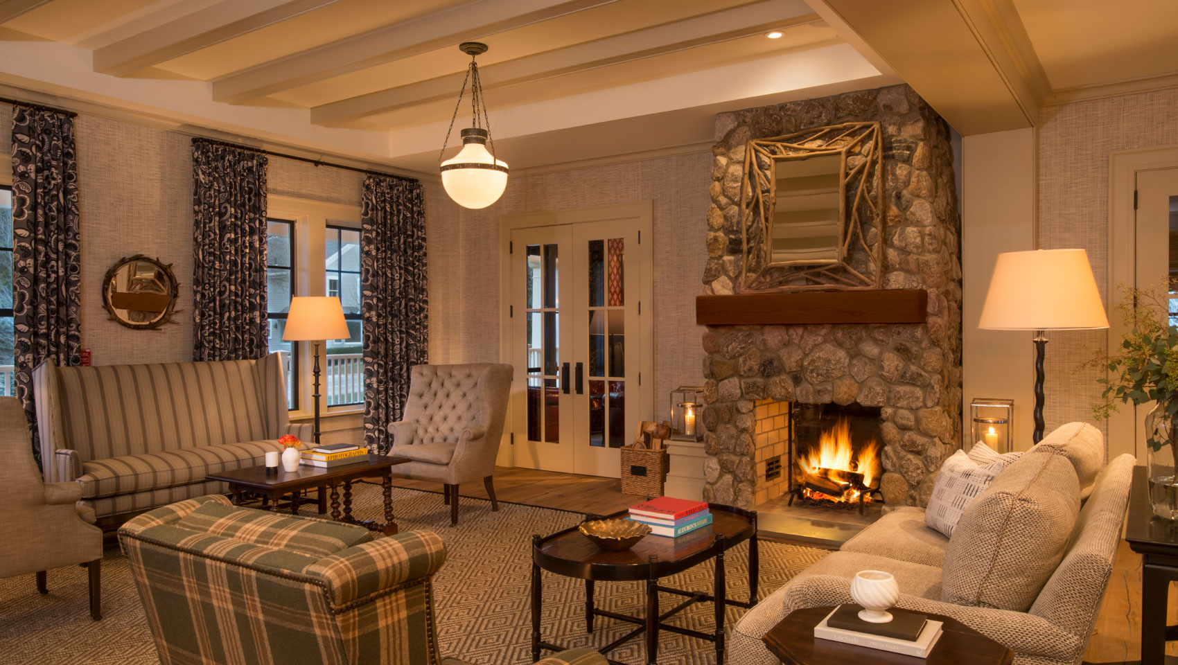 Inviting living room with a lit stone fireplace, various upholstered seating, patterned curtains, and a central chandelier