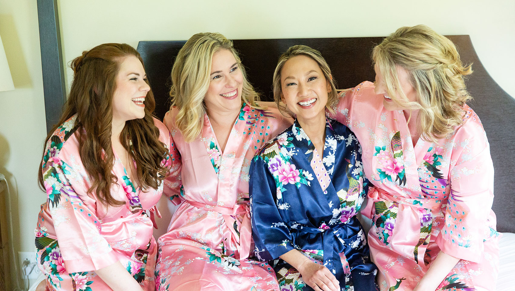 Bride posing with bridesmaids on bed in robes